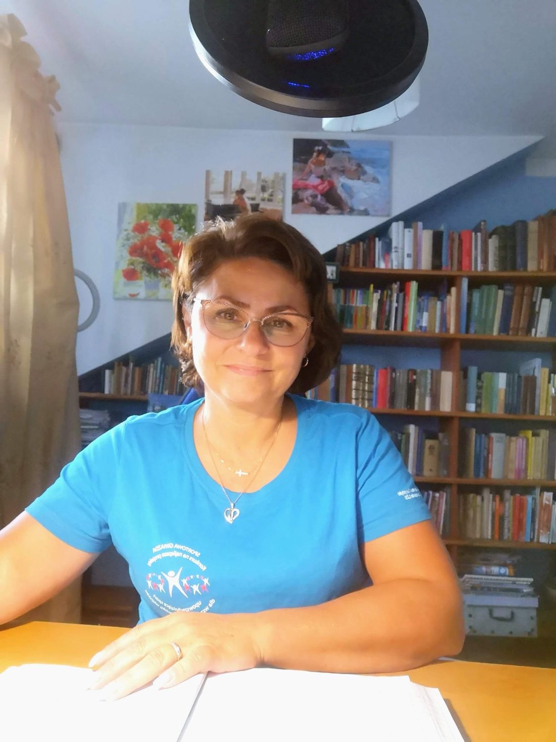 Jolanta Sobowska за столом перед онлайн уроком, на тлі книжкові полиці
